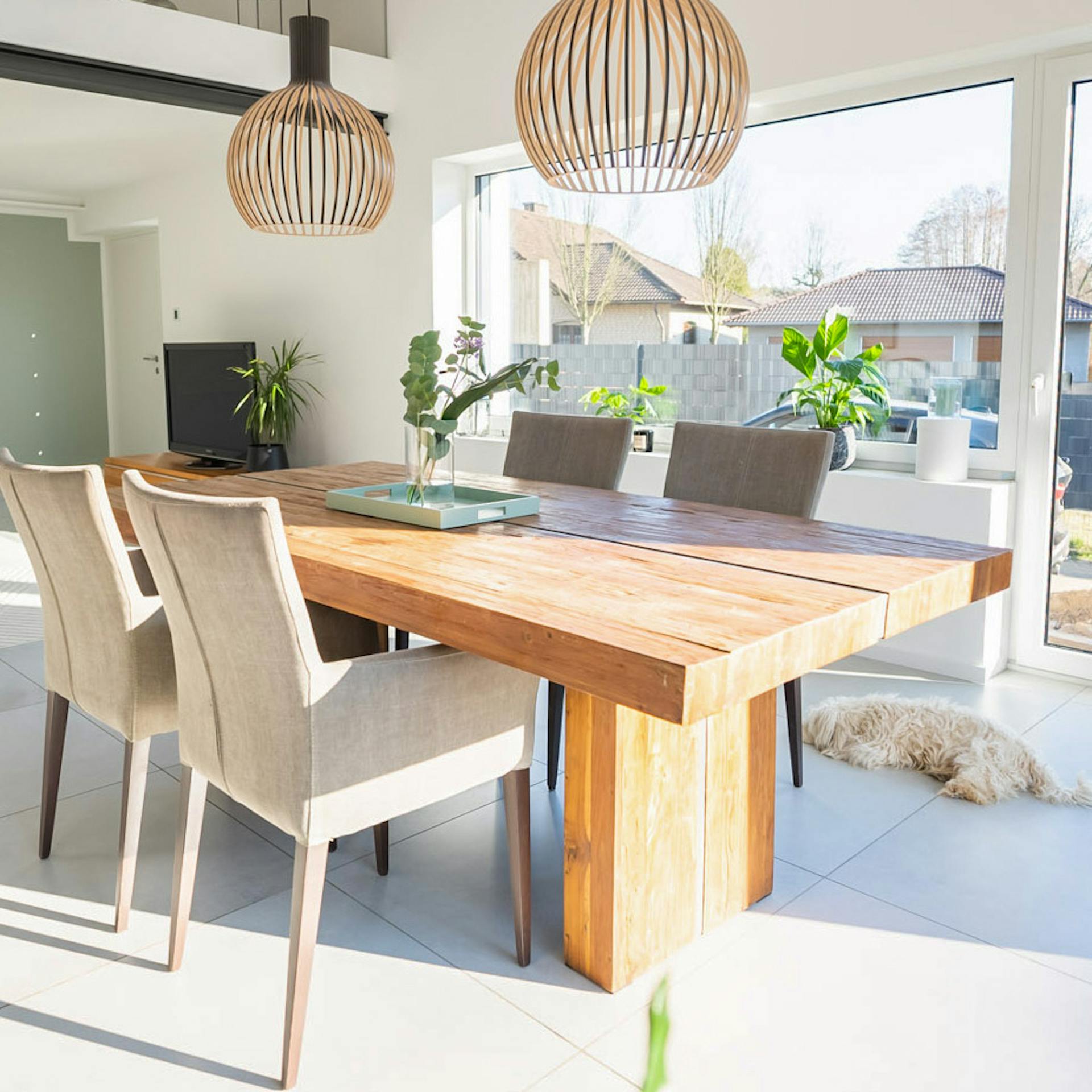 Massivholz-Esstisch, beige Polsterstühle, durchbrochene Hängelampen über dem Esstisch, modernes Wohnzimmer