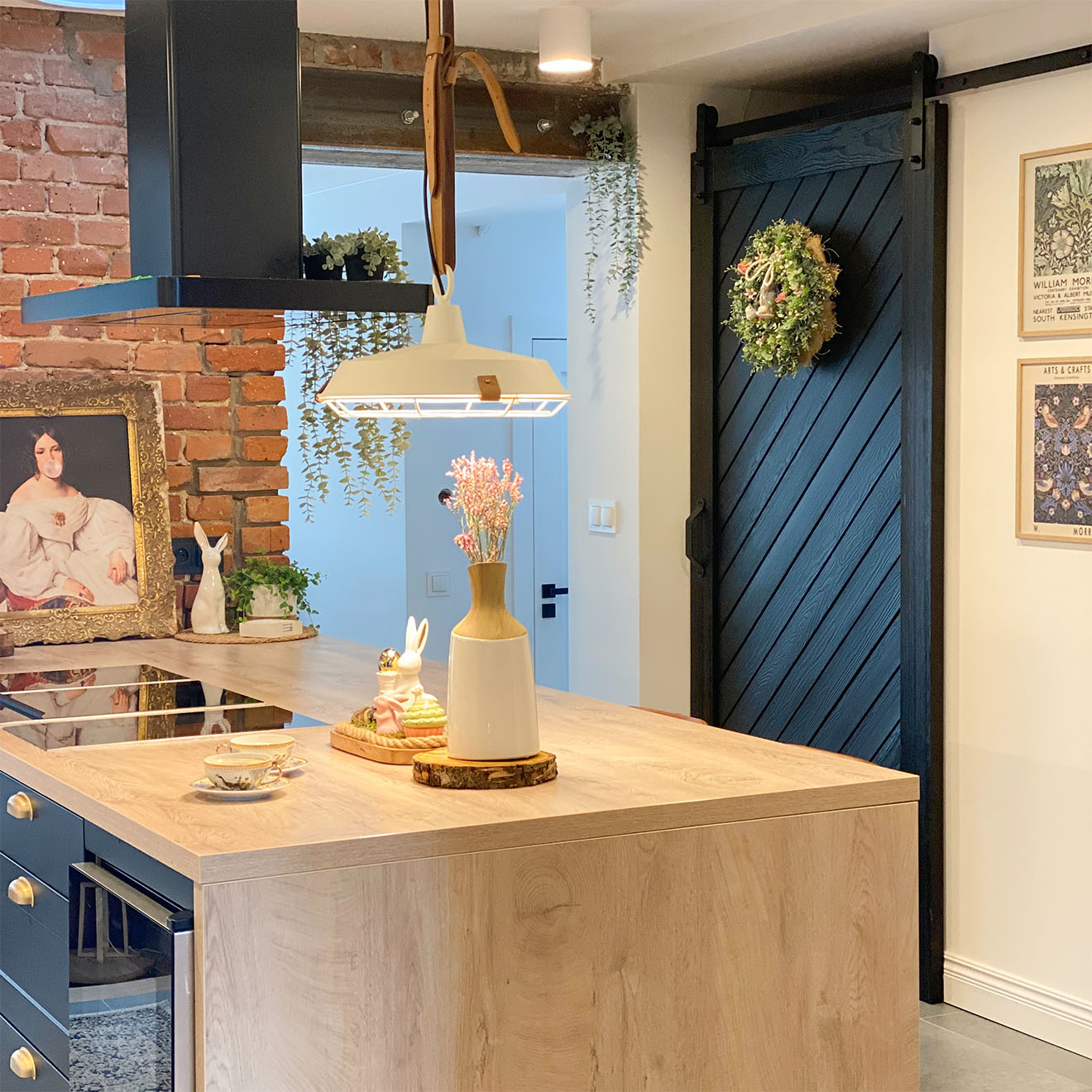 große Kücheninsel mit Holzplatte, schwarze Haube über der Kücheninsel, Schiebetür zur Speisekammer, dekorativer Kranz an der Tür