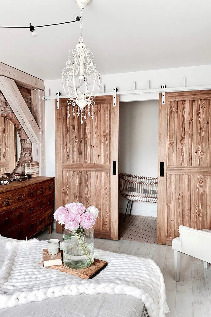 hölzerne Schiebetüren, wechselseitige Schiebetüren, rustikaler Stil in Innenräumen, Modern-Rustic-Stil, Türen im „Barn Door“-Stil, weißes Schiebesystem, Schiebesystem für wechselseitige Türen, weißer rustikaler Kronleuchter, Ziegelwand im Schlafzimmer