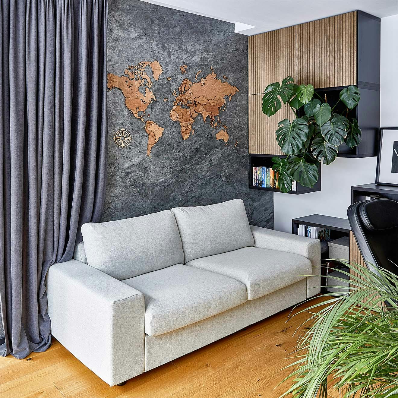 jasnoszara sofa przy ścianie udekorowanej fornirem kamiennym oraz drewnianą mapą świata