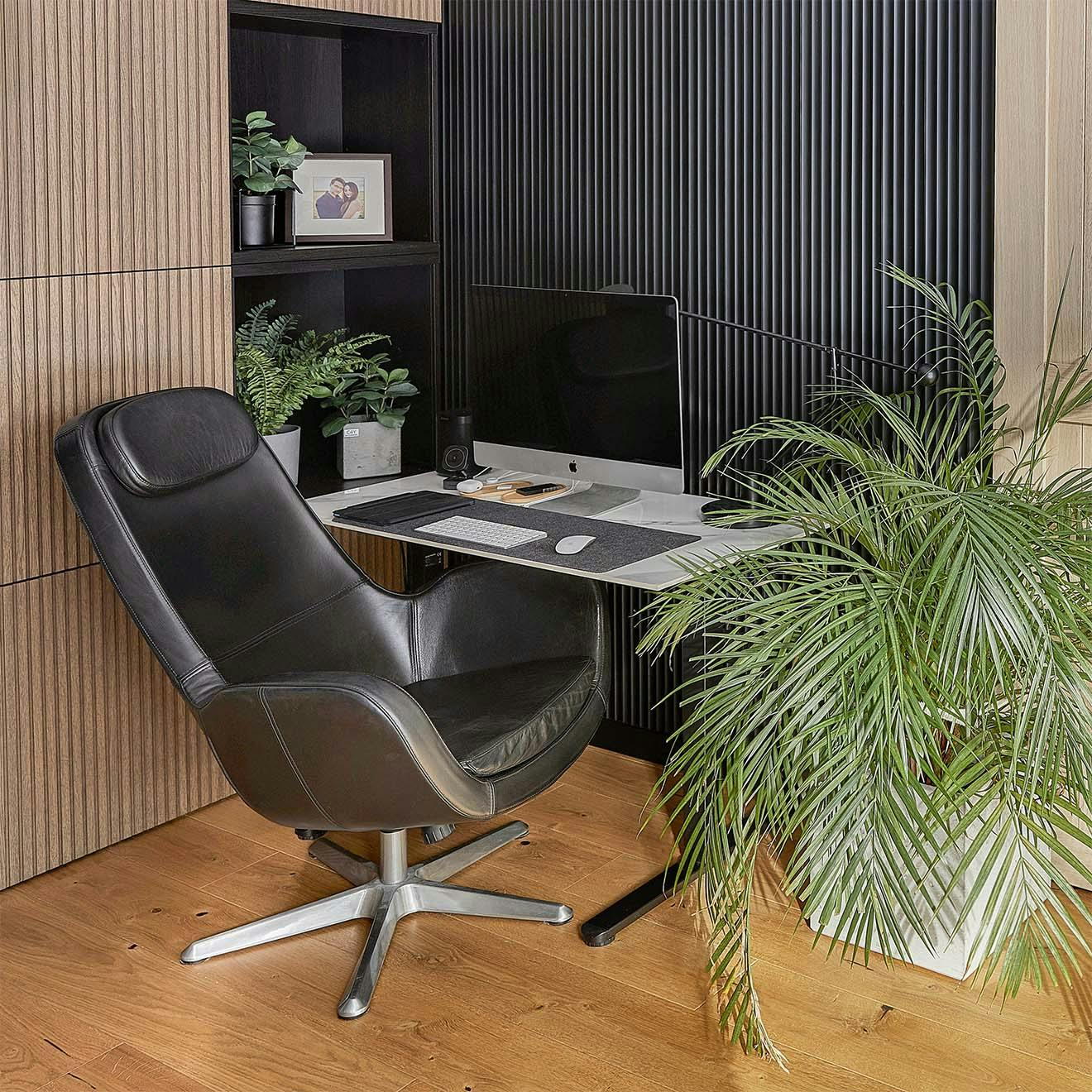 schwarzer Ledersessel, kleiner Schreibtisch, große Topfpflanze und schwarze Wandlamellen im Homeoffice