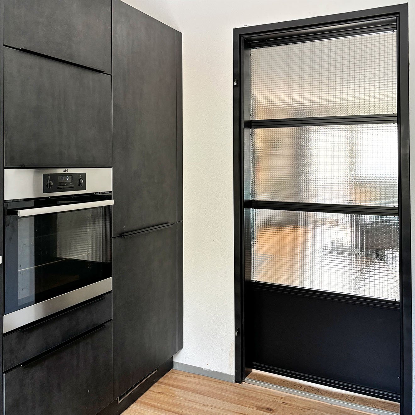 nowoczesna kuchnia z czarnymi szafkami i wbudowanym piekarnikiem obok przesuwnych drzwi ze stali i szkła zbrojonego