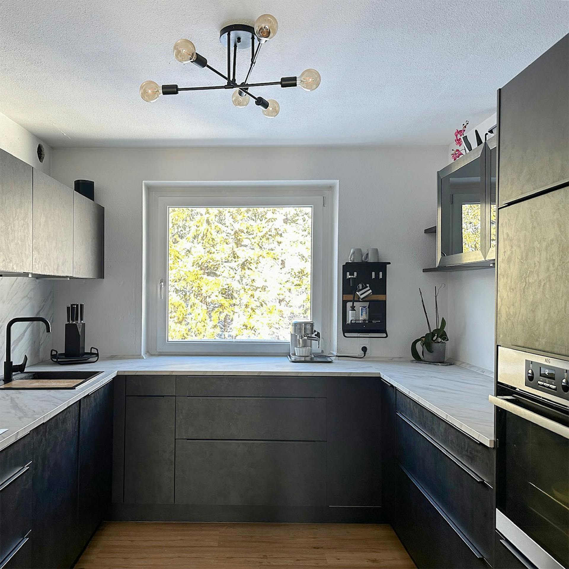 współczesna, minimalistyczna kuchnia z czarnymi szafkami, białymi ścianami i dużym oknem