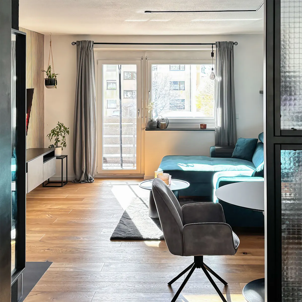 minimalistyczne mieszkanie z przestronnym salonem, w którym znajdują się turkusowa sofa, czarny stół i szare fotele