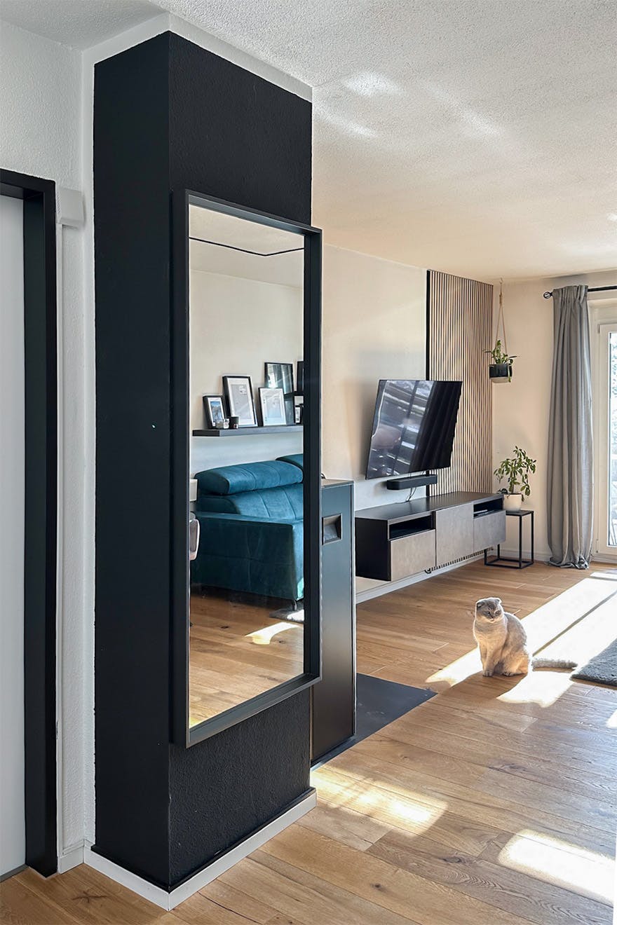 duże lustro na czarnej ścianie w salonie z jasną, drewnianą podłogą oraz turkusową sofą