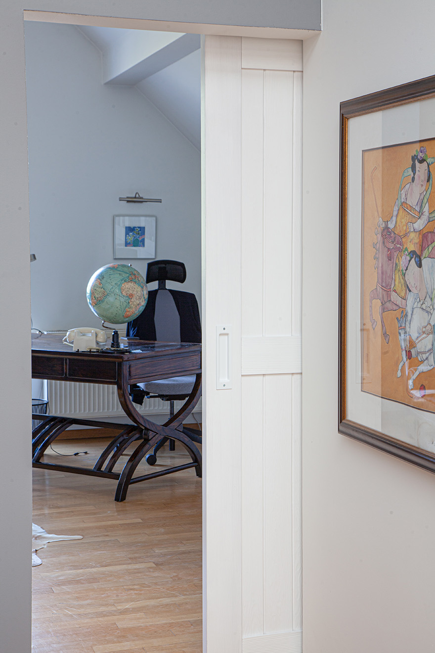 eine offene weiße Tür, die einen Teil eines Arbeitszimmers mit einem dunklen Schreibtisch freigibt