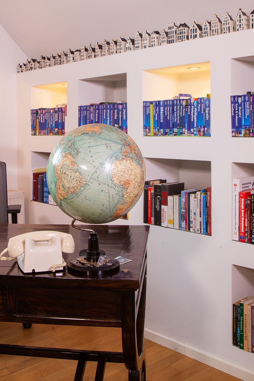 ein Globus und ein Telefon auf einem dunkelbraunen Schreibtisch neben einer Wand mit Regalen voller Bücher