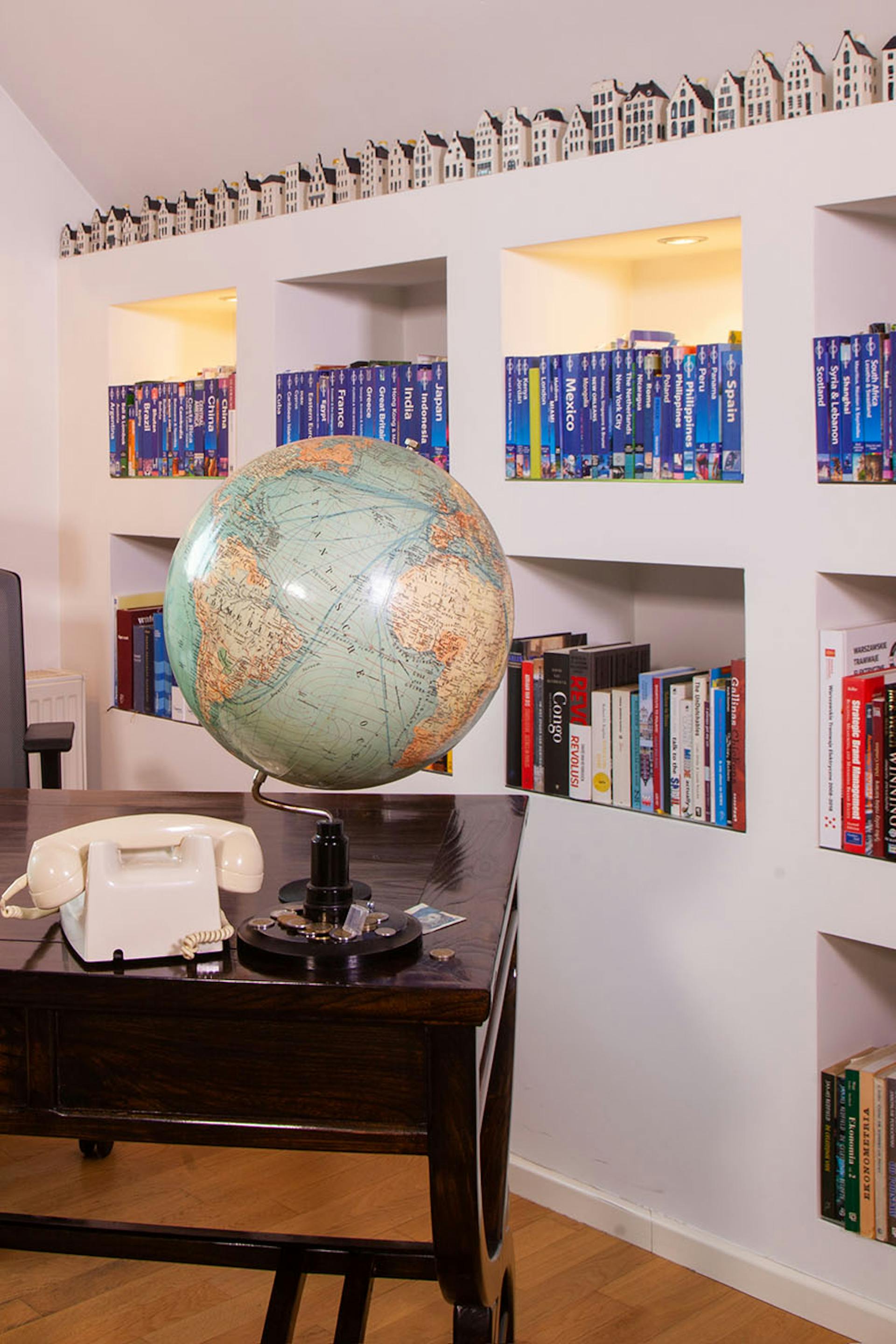 ein Globus und ein Telefon auf einem dunkelbraunen Schreibtisch neben einer Wand mit Regalen voller Bücher