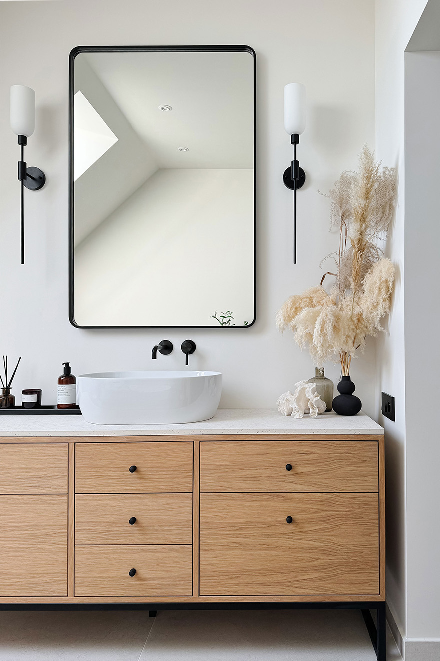 ein rechteckiger Spiegel mit einem zarten schwarzen Rahmen, der über einem Holzschrank mit Waschbecken hängt