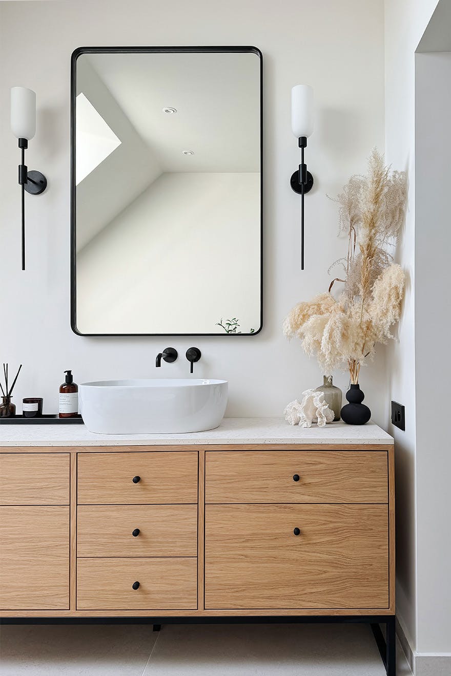 ein rechteckiger Spiegel mit einem zarten schwarzen Rahmen, der über einem Holzschrank mit Waschbecken hängt
