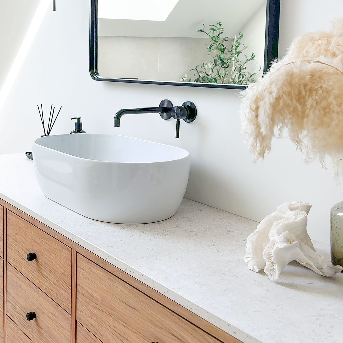 weißes ovales Aufsatzwaschbecken mit schwarzen Armaturen auf einem Holzschrank
