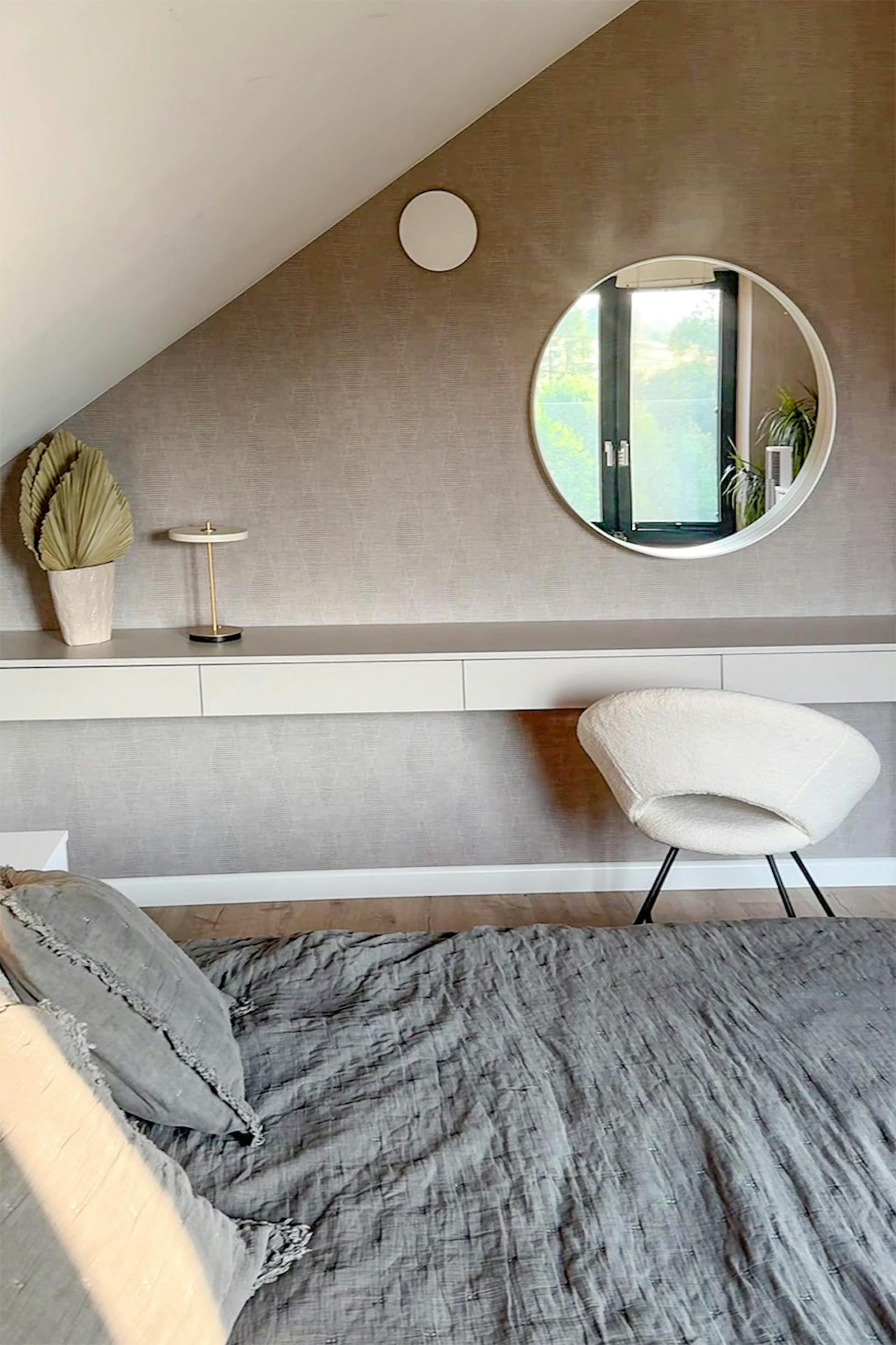 łóżko z szarą narzutą i toaletka w minimalistycznej sypialni ze skośnym sufitem