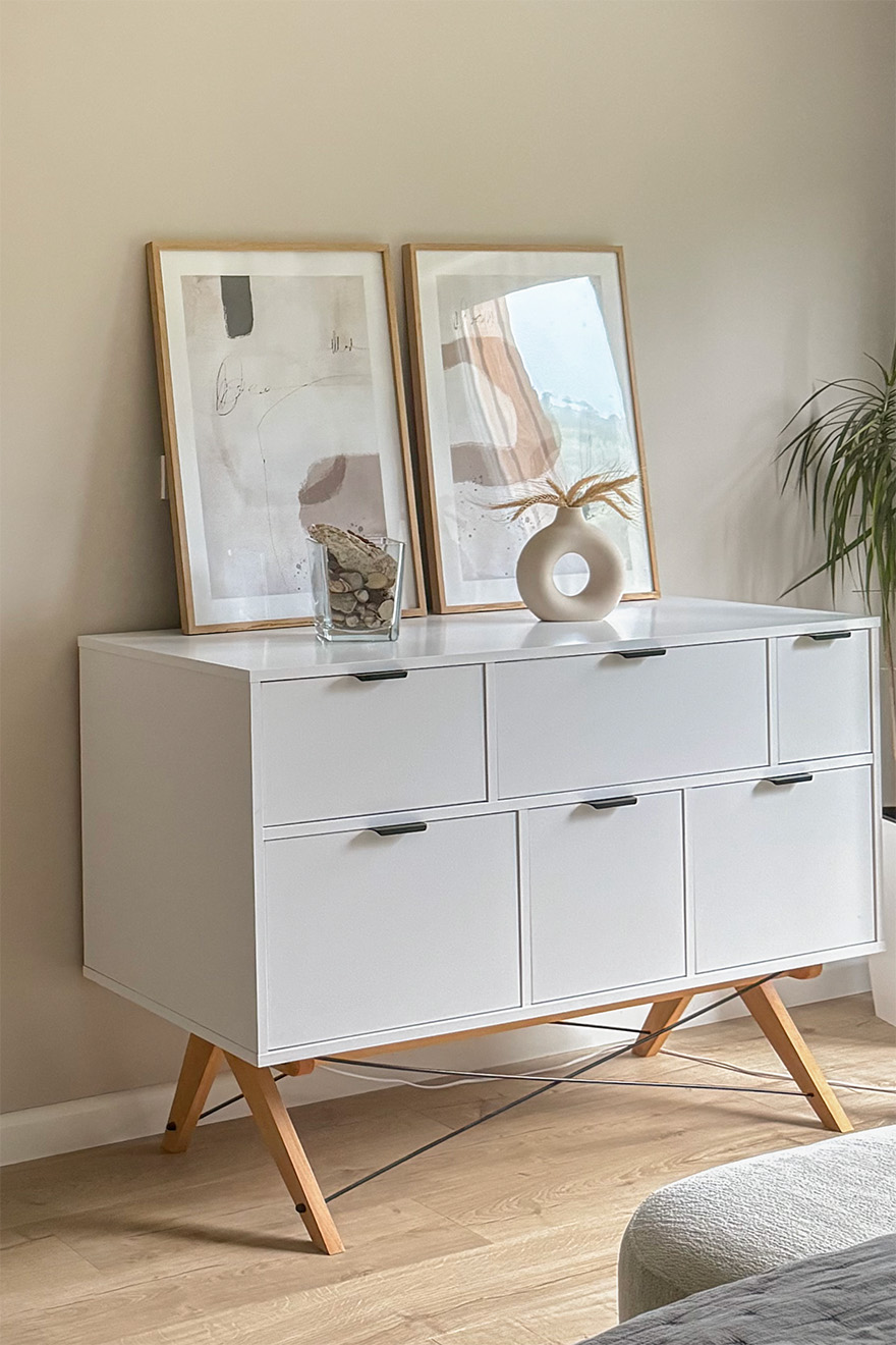 Gerahmte Poster auf einer weißen Kommode mit tiefen Schubladen