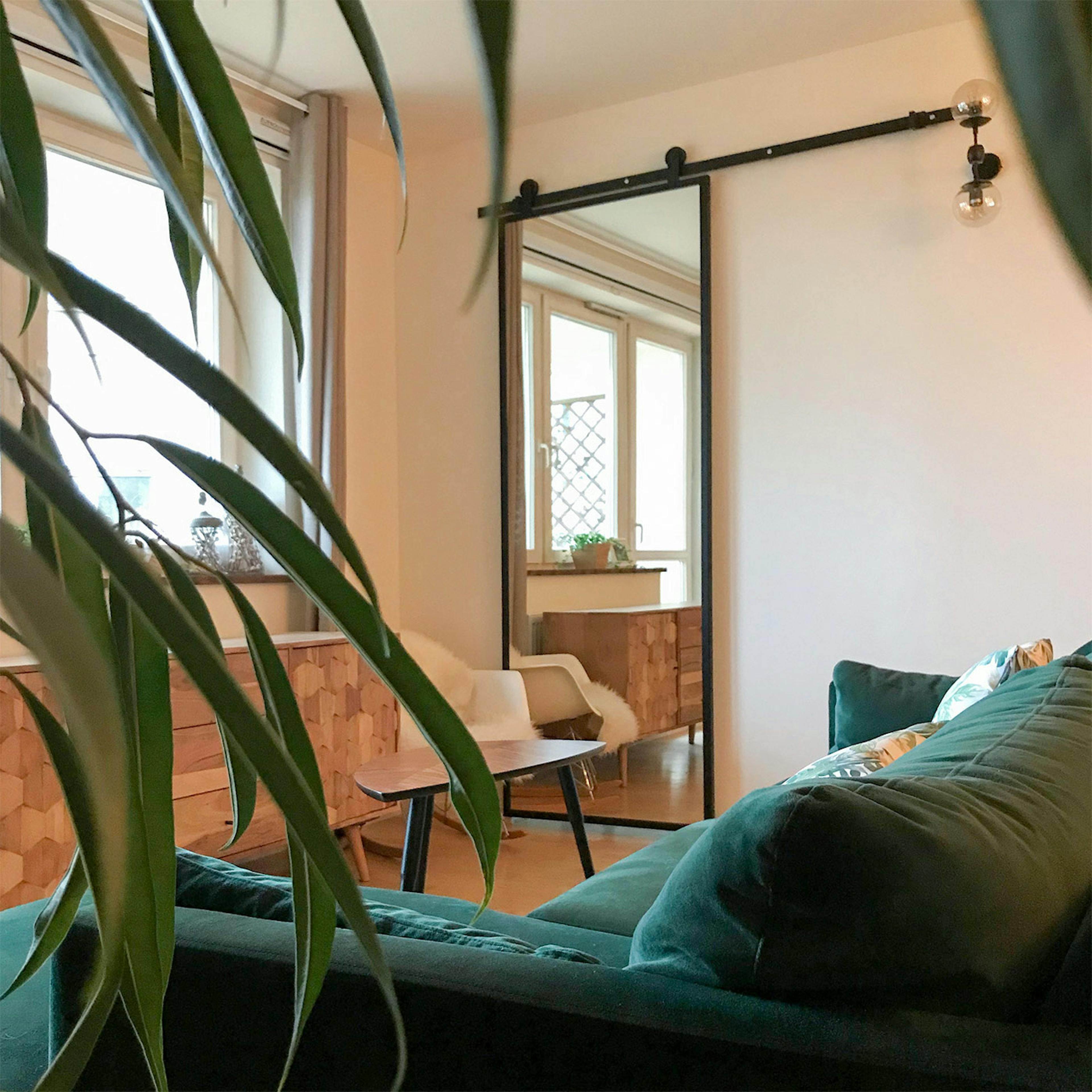 drzwi przesuwne z lustrem, drzwi z lustrem w metalowej ramie, drzwi przesuwne w nowoczesnym wnętrzu, zielona sofa, duże lustro w salonie