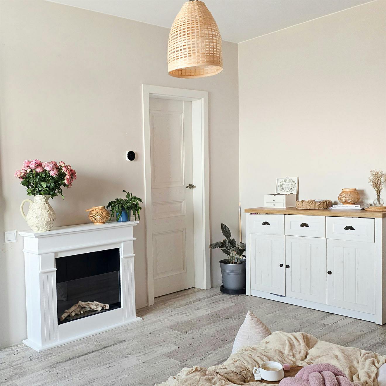 detale sypialni: biała komoda drewniana, kominek, pleciona lampa, naturalne dekoracje na kominku i komodzie