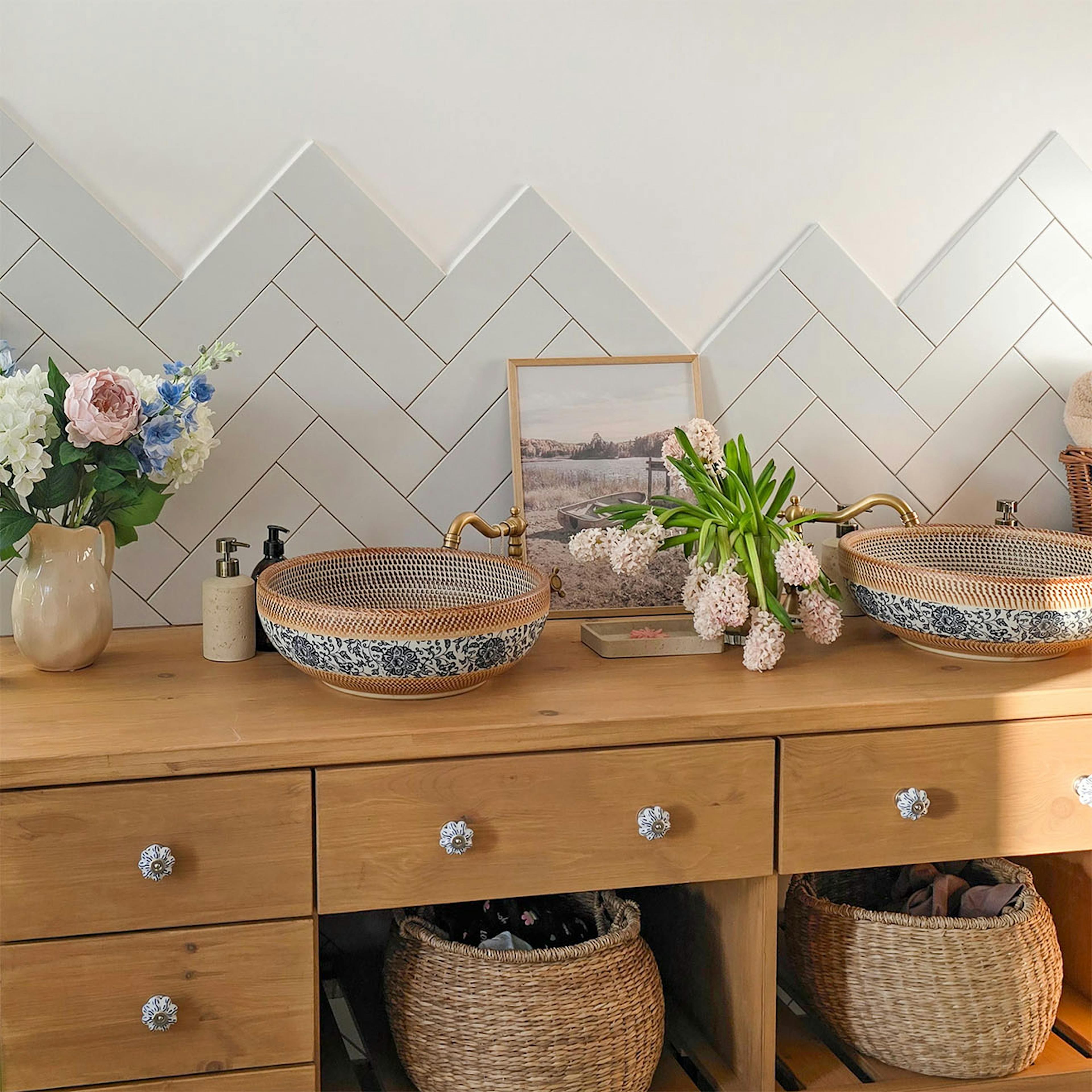 okrągłe ceramiczne umywalki nablatowe z ozdobnymi wzorami i z retro mosiężną armaturą przy ścianie z płytkami ułożonymi w jodełkę