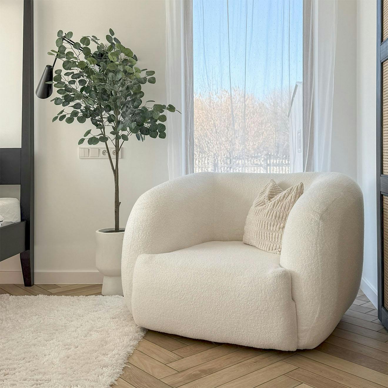 ein gemütlicher weißer Sessel mit strukturiertem Kissen steht neben einem weichen weißen Teppich und einer Topfpflanze