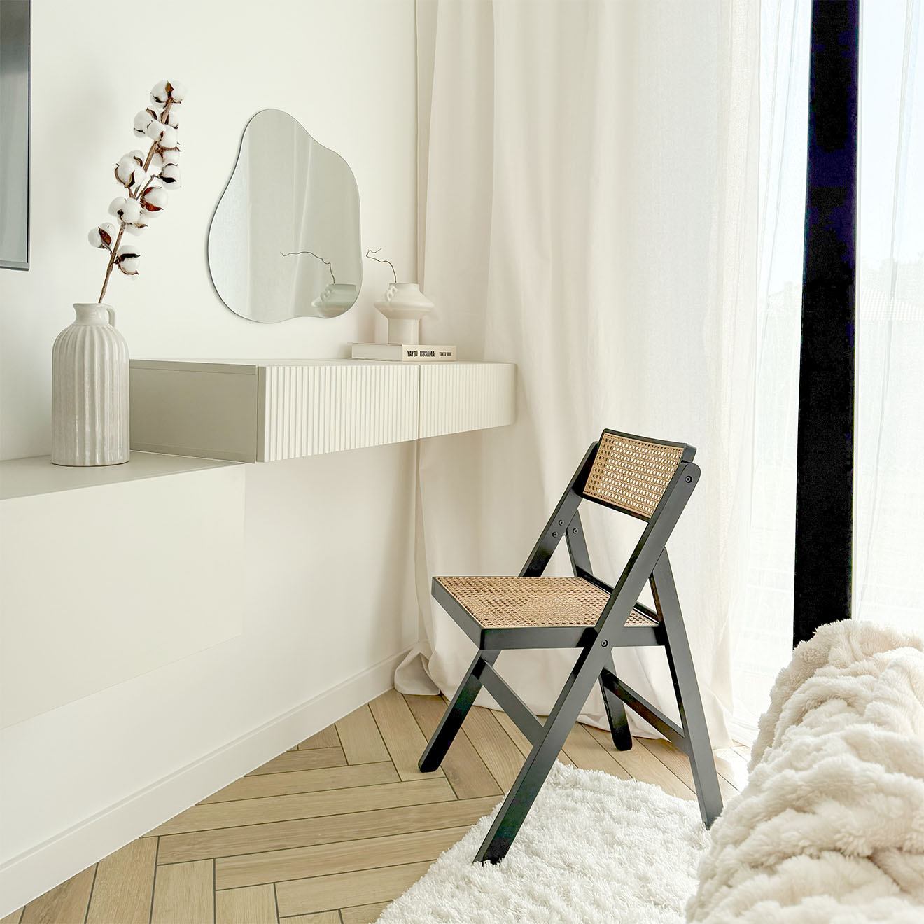 minimalistischer Schminktisch mit einem einzigartig geformten Wandspiegel und einem stilvollen schwarzen Klappstuhl mit Rattansitz