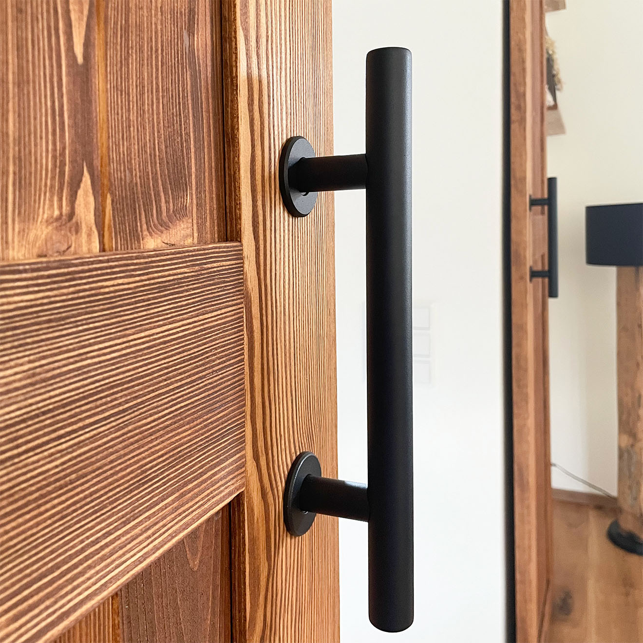 Detal czarnego, metalowego uchwytu na drewnianych, rustykalnych drzwiach przesuwnych.