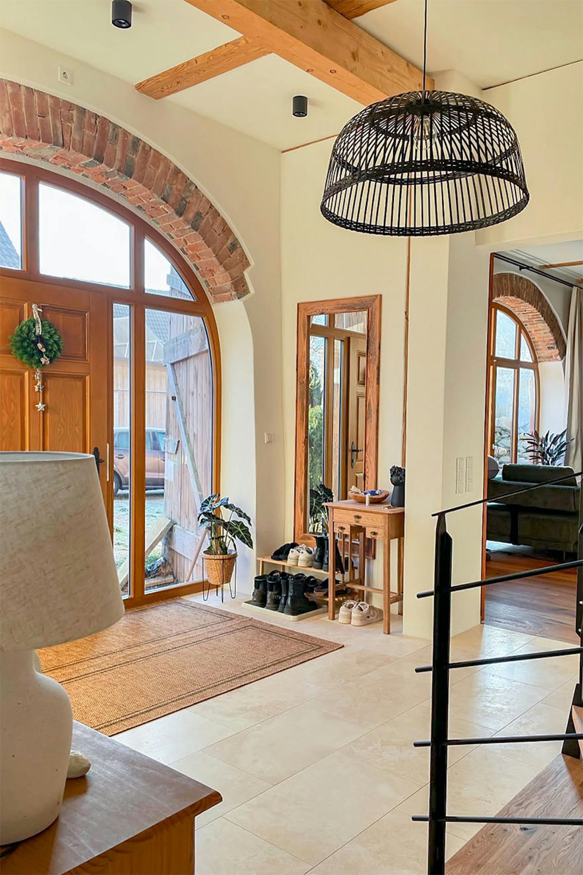 Moderner Eingangsbereich im Landhausstil mit beigefarbenen Fliesen, großen gewölbten Türen und Fenstern, einer Hängelampe und Holzakzenten.