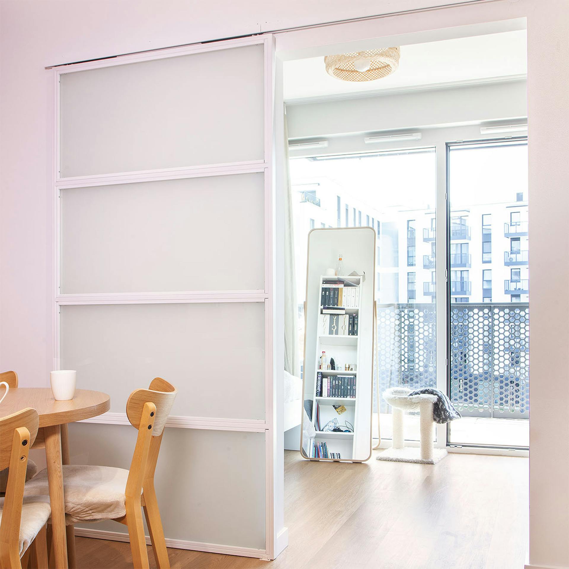 Otwarte, białe drzwi przesuwne z mlecznym szkłem, ukazujące fragment jasnego pokoju z dużym stojącym lustrem i drapakiem dla kota.