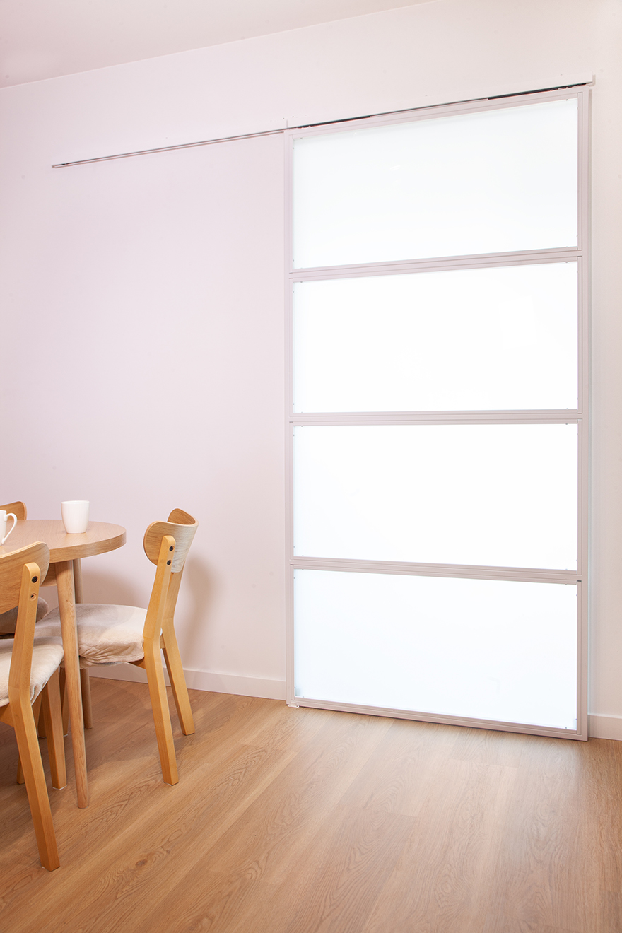 Geschlossene weiße Schiebetüren mit vier Milchglas-Paneelen neben einem runden Tisch mit Holzstühlen.