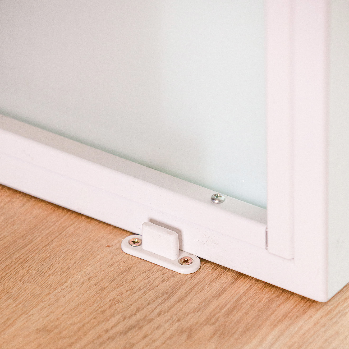 Detail einer weißen Bodenführung an der unteren Kante einer weißen Schiebetür, befestigt am Holzboden.