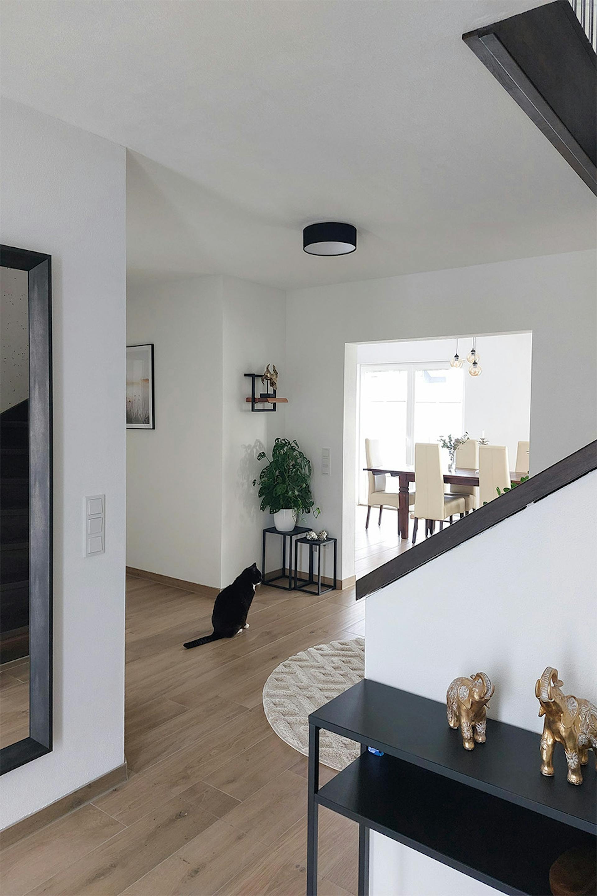 Przedpokój w nowoczesnym domu z jasną podłogą. Widok na jadalnię z drewnianym stołem i kremowymi krzesłami.