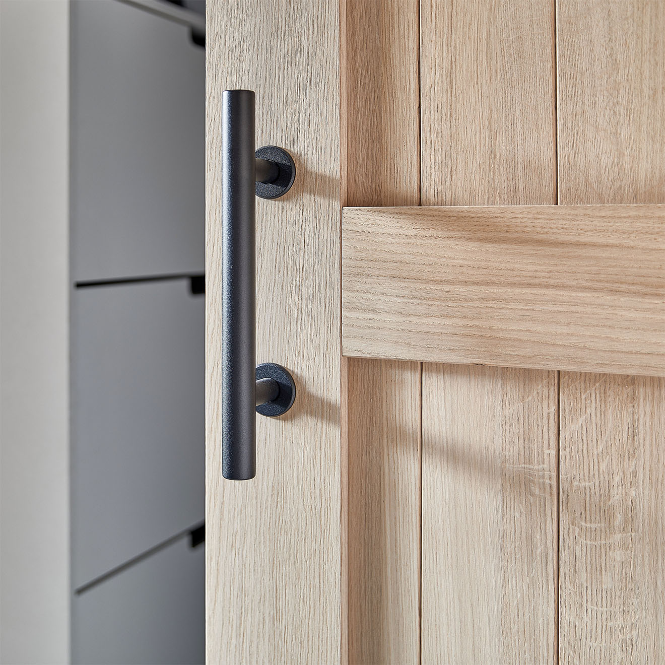 Detal czarnego uchwytu do dębowych drzwi przesuwnych. Uchwyt w kształcie prostej, matowej rurki podkreśla nowoczesny, minimalistyczny styl.