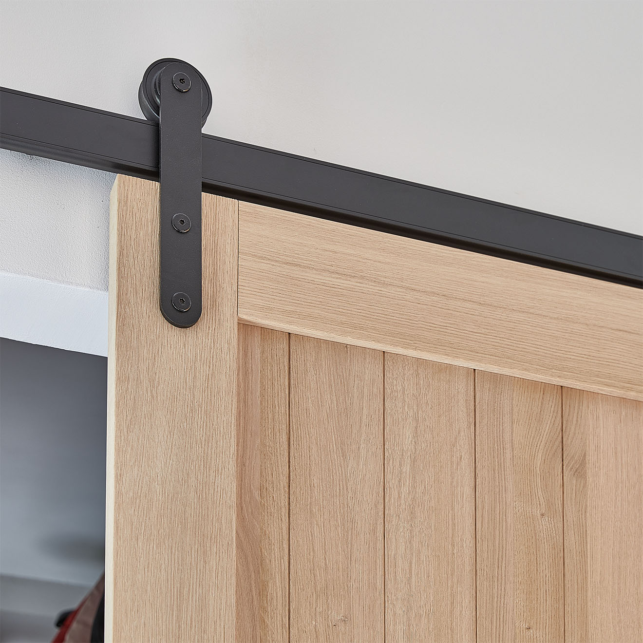 Eine Nahaufnahme des schwarzen Schiebesystems (Beschläge) und des oberen Teils der Eichentür. Das schwarze System kontrastiert mit dem natürlichen, hellen Holz der Eichentür und schafft so eine harmonische Mischung aus industriellem und natürlichem Stil.