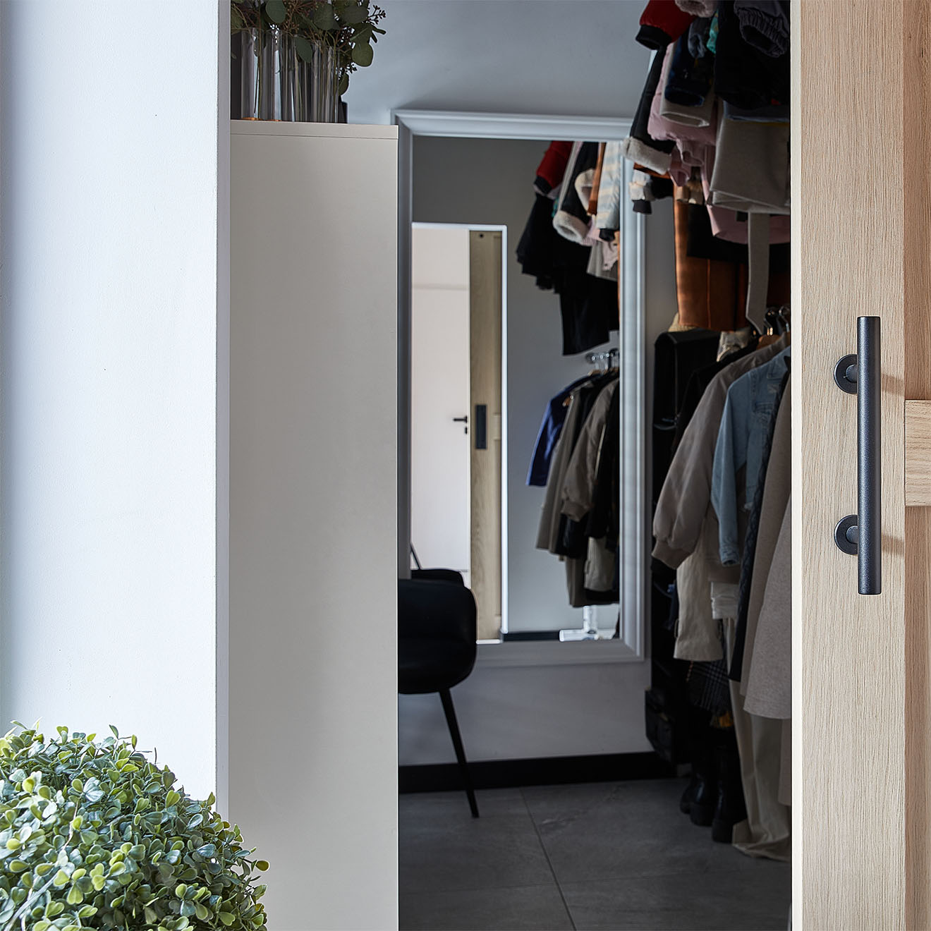 Detail der Schiebetüren aus Eichenholz, die sich öffnen lassen und den Blick auf das Innere des Ankleides freigeben. Im Inneren sind auf Kleiderbügeln hängende Kleidungsstücke und ein Spiegel zu sehen.