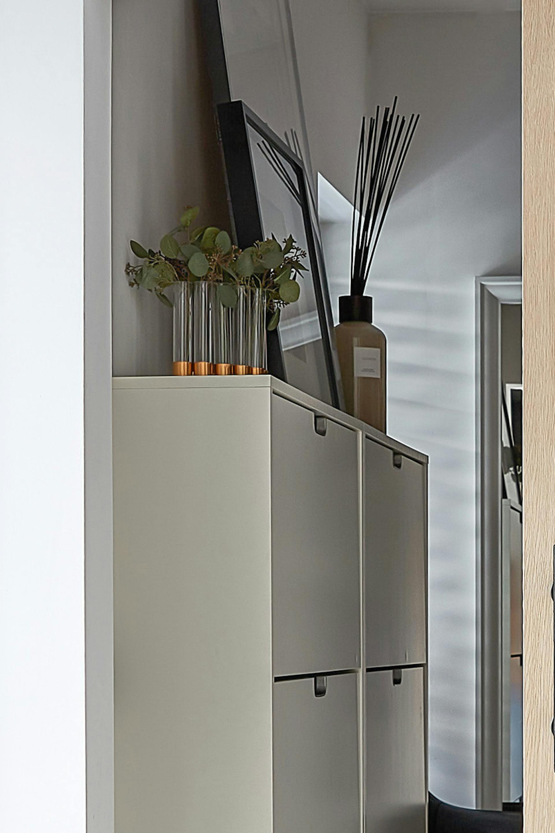 Details des begehbaren Ankleide, sichtbar durch die angelehnte Eichentür. Auf einem weißen Schuhschrank thront stilvolle Dekoration: eine Vase mit Kräutern und ein Duftzerstäuber, die dem Raum eine gemütliche und elegante Atmosphäre verleihen.