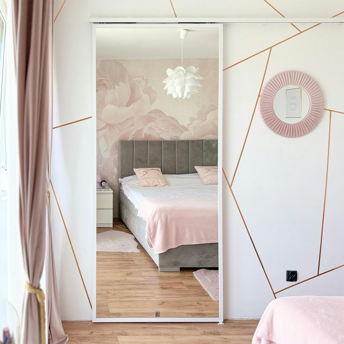 Nowoczesna sypialnia w pudrowym różu i szarości; Duże lustro na drzwiach przesuwnych; Fototapeta z różami za łóżkiem; Złote linie geometryczne na ścianie.