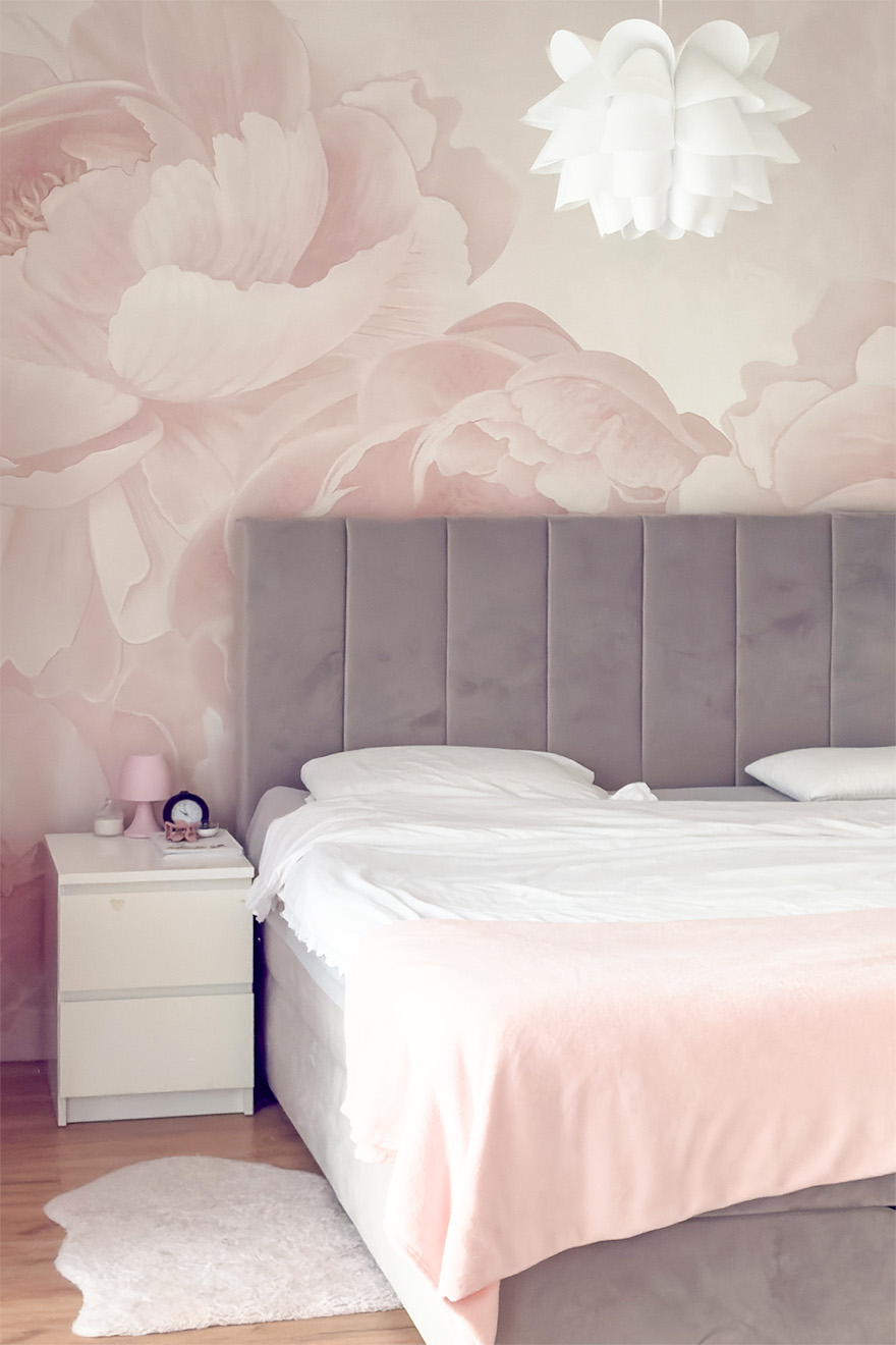 Bett mit grauem, gestepptem Kopfteil; Fototapete mit großen rosa Blumen im Schlafzimmer; weißer Nachttisch.