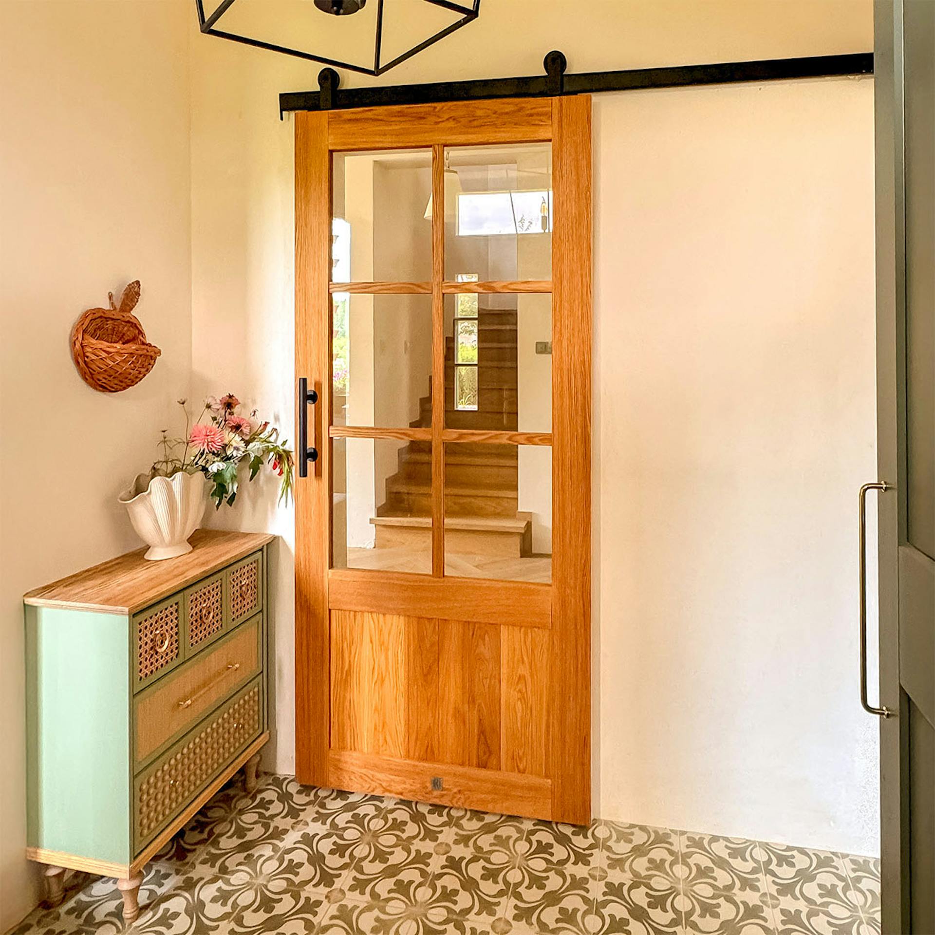 Przeszklone drzwi przesuwne z dębu w aranżacji wiatrołapu z szałwiową komodą i wzorzystymi płytkami.