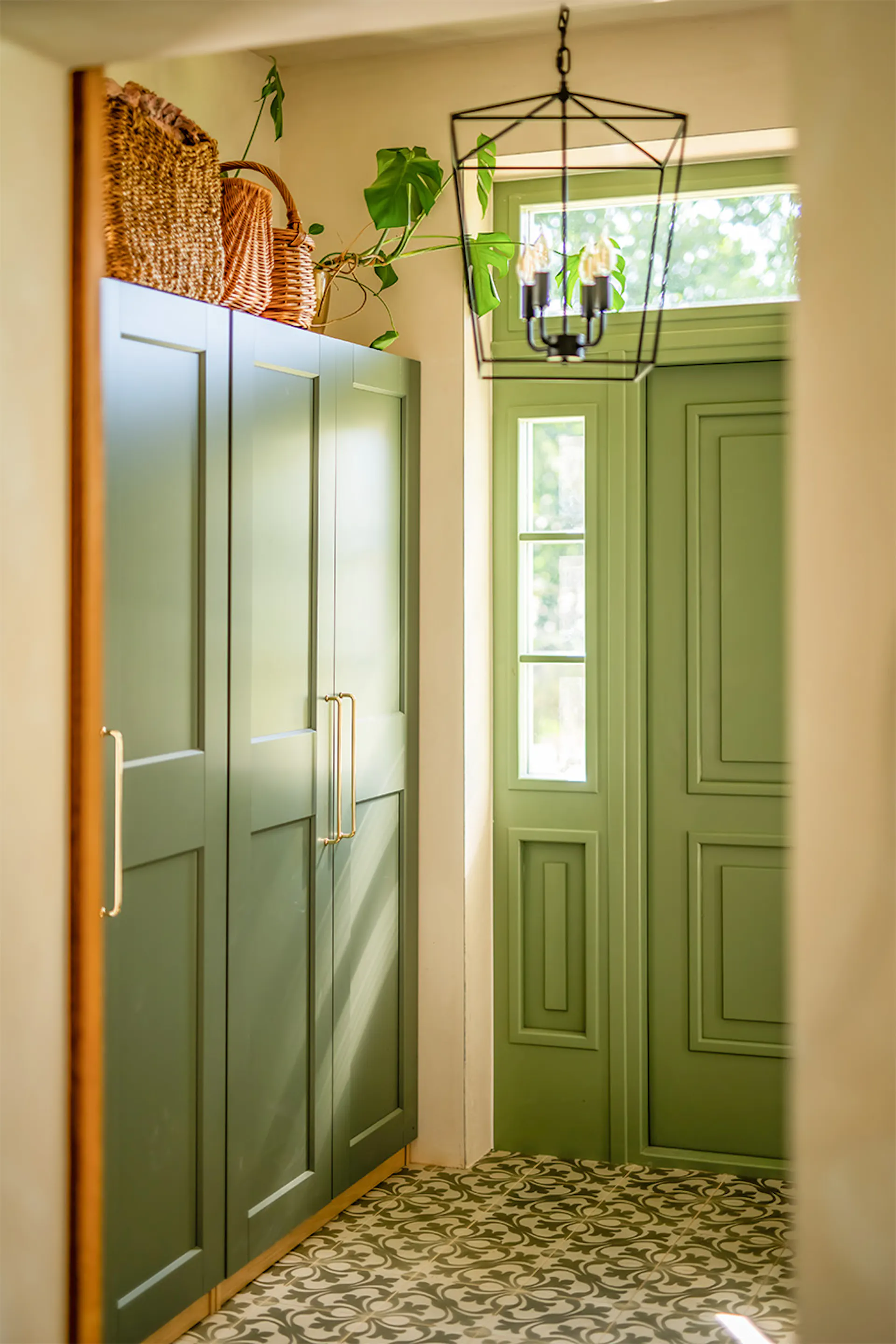 Wnętrze wiatrołapu w stylu modern farmhouse: szałwiowe szafy w zabudowie, zielone drzwi wejściowe i wzorzysta posadzka.