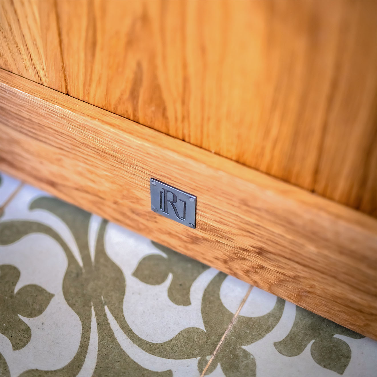 Detal dolnej części dębowych drzwi ukazujący usłojenie drewna na tle wzorzystych płytek podłogowych.