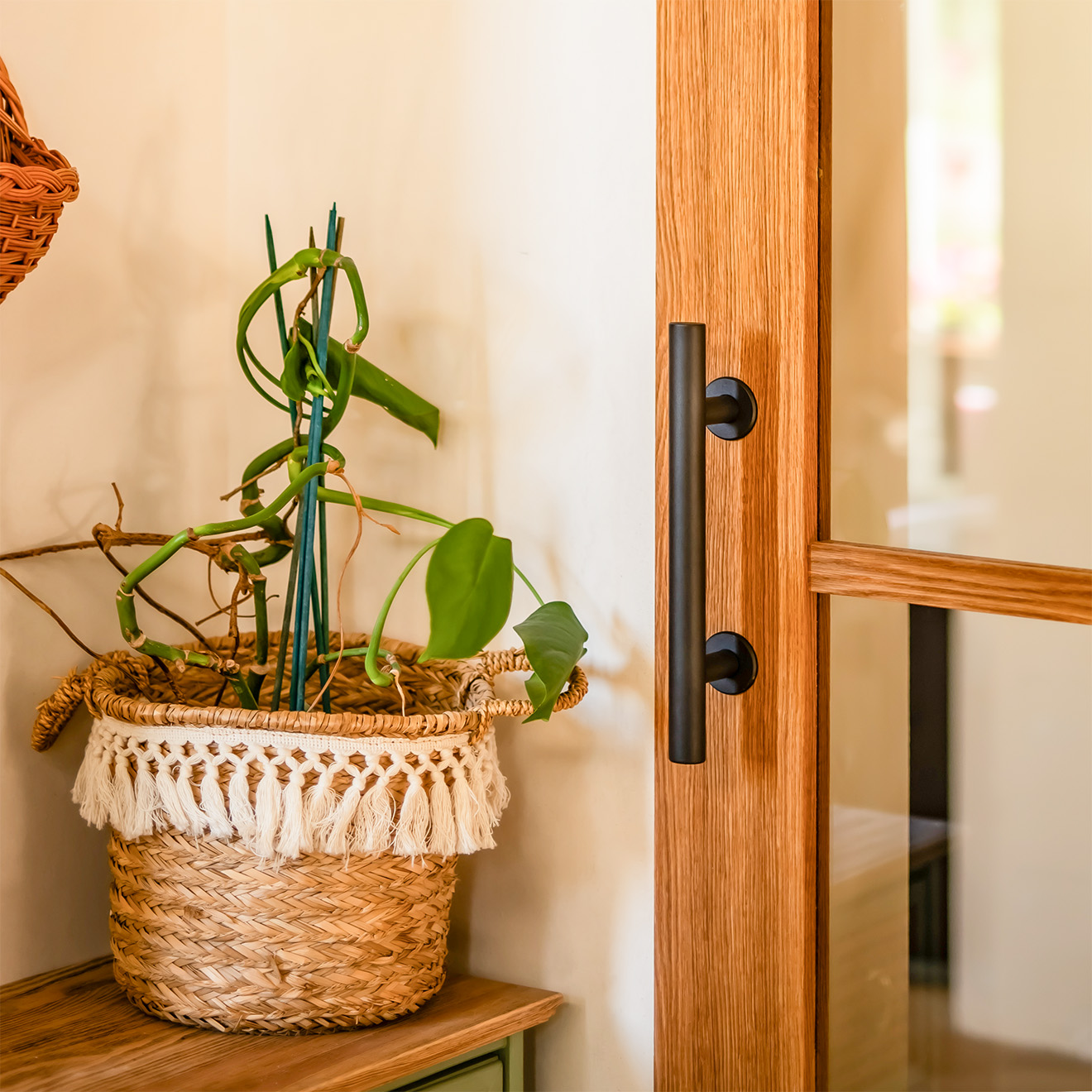 Czarny uchwyt na dębowych drzwiach przesuwnych obok dekoracji w koszu plecionym na drewnianej komodzie.