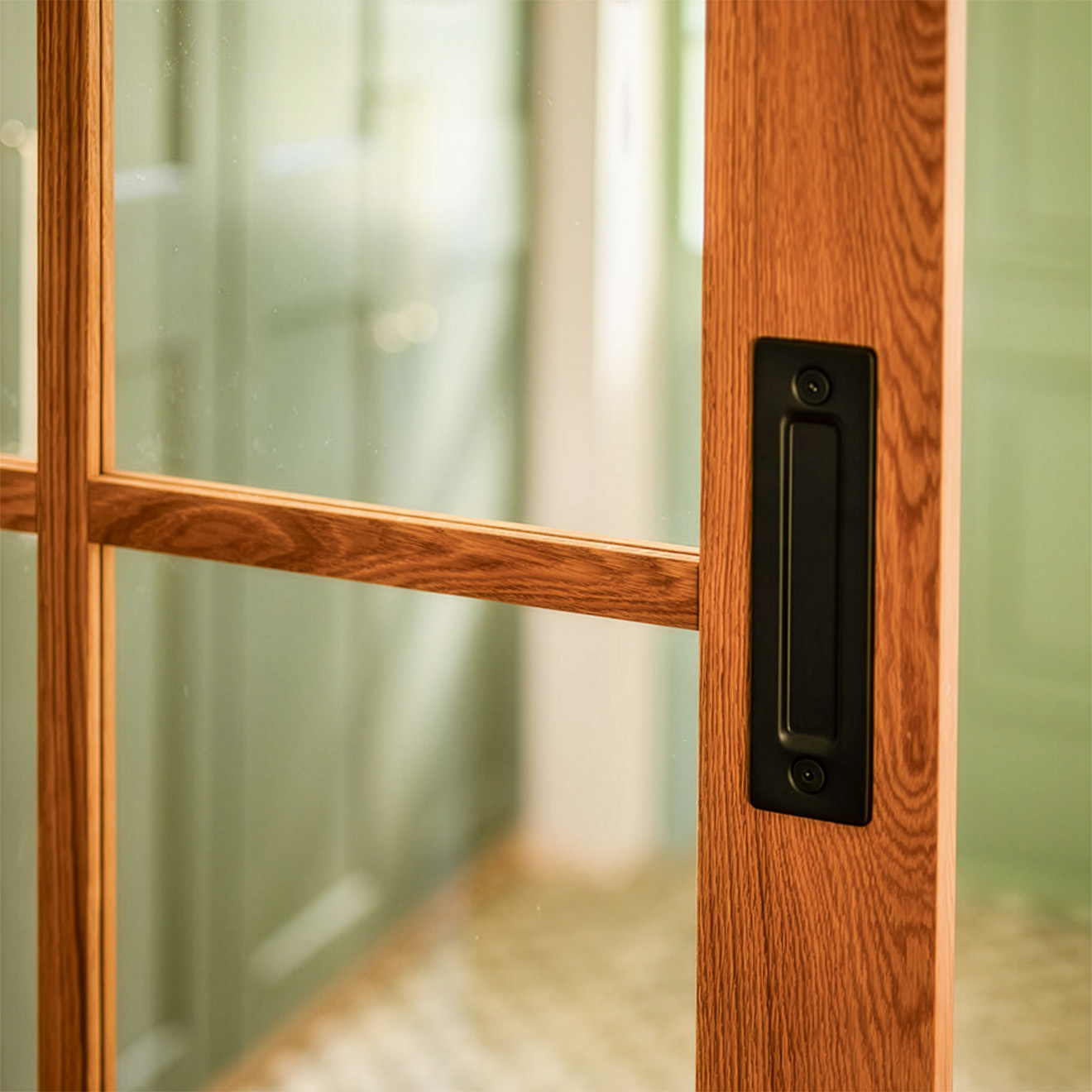 Detal dębowych drzwi przesuwnych w stylu modern farmhouse: czarny matowy uchwyt wpuszczany, widoczne słoje drewna oraz przeszklenia ze szprosami.