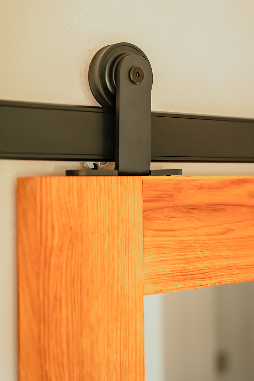 Nahaufnahme eines schwarzen Schiebetürsystems, das an der Oberkante einer Eichentür montiert ist.