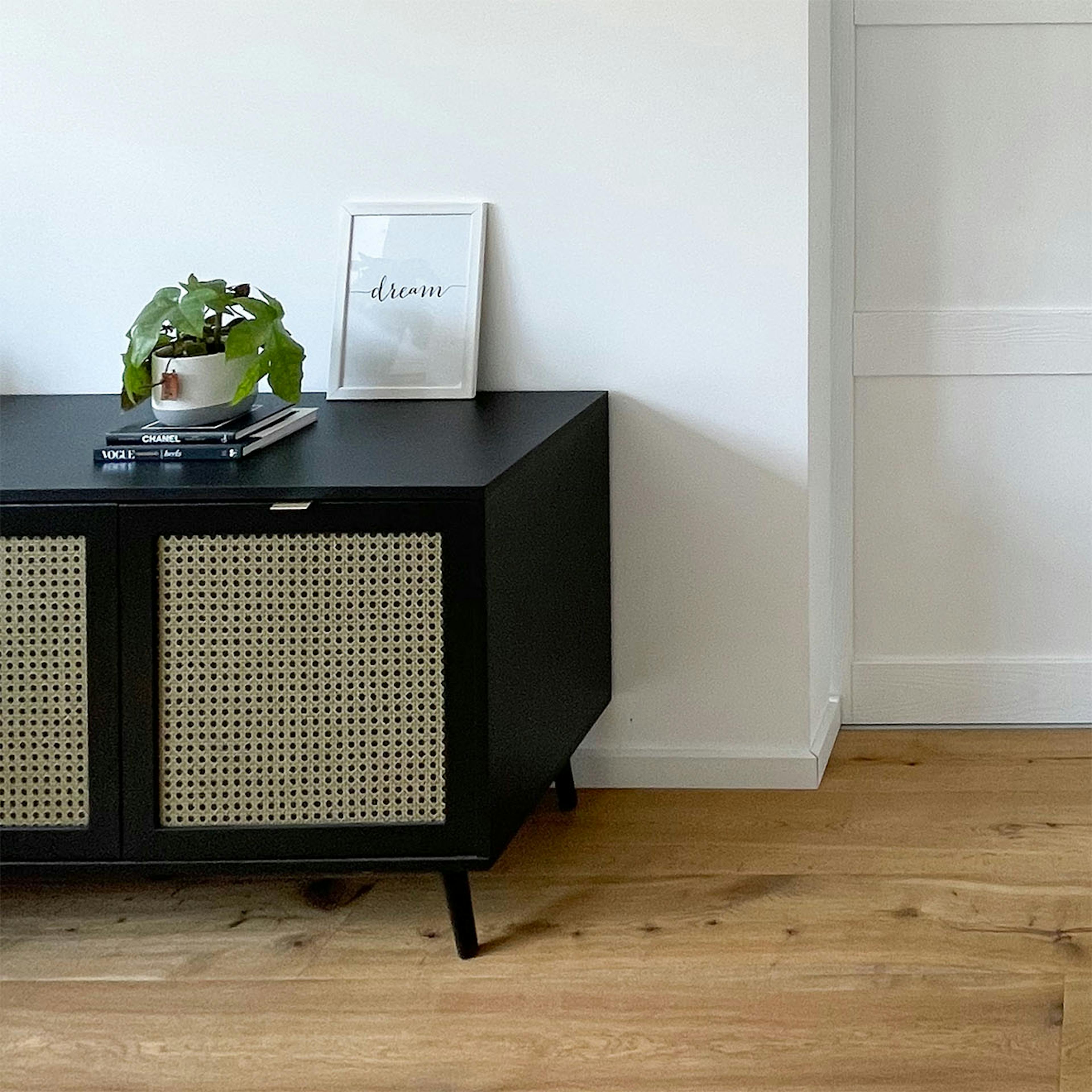 Schwarze niedrige Kommode mit Rattan auf weißem Wandhintergrund