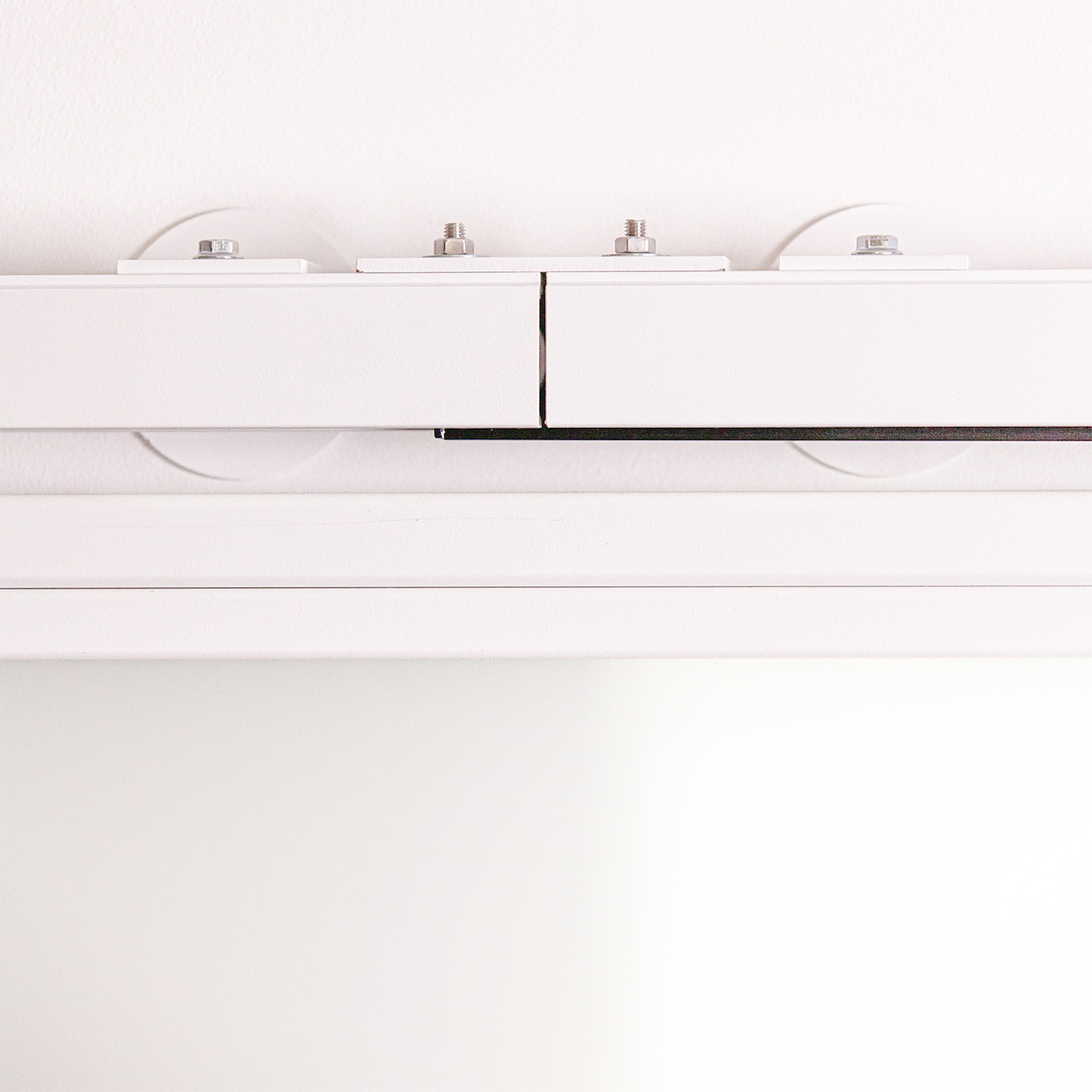 Zbliżenie na białą szynę systemu TOP WALL z widocznymi punktami montażowymi do ściany.