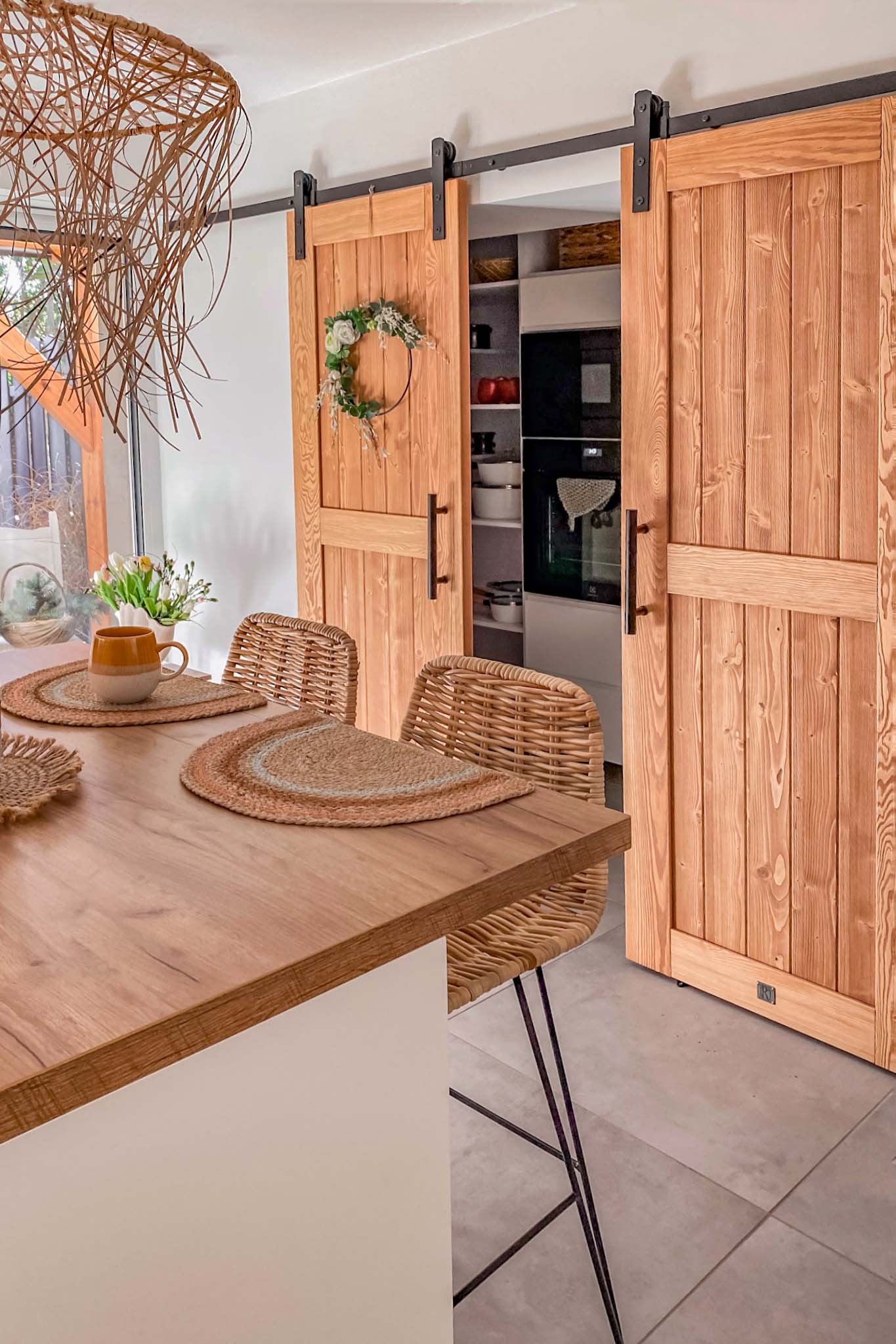 Deckenleuchte mit durchbrochenem Lampenschirm aus Bast, Kücheninsel, doppelte Holzschiebetüren, die die Nische in der Küche schließen, Barhocker aus Korbgeflecht, geflochtene Untersetzer