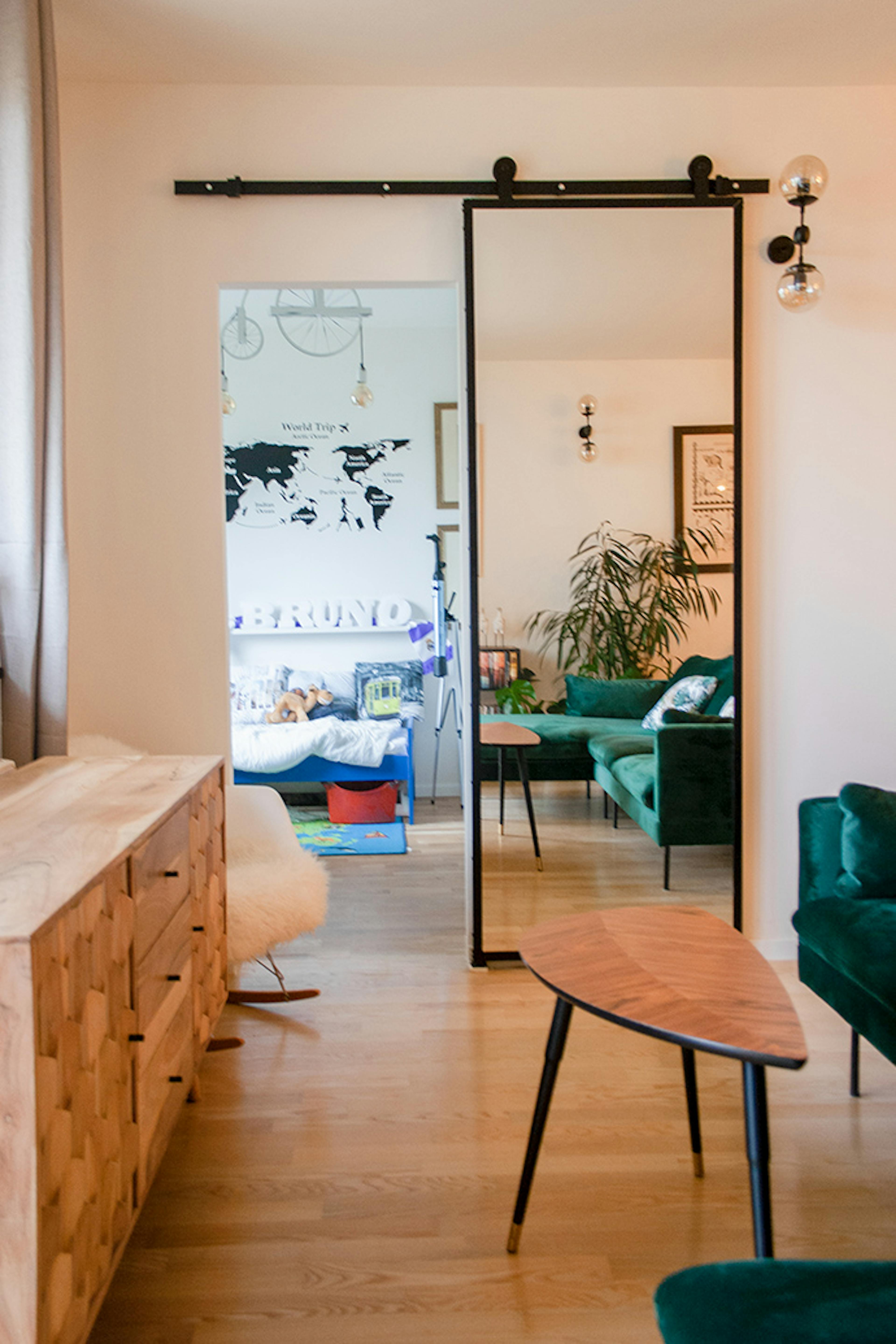 drzwi przesuwne z lustrem, drzwi z lustrem w metalowej ramie, drzwi przesuwne w nowoczesnym wnętrzu, zielona sofa, komoda w stylu nowoczesnym, stolik w stylu skandynawskim