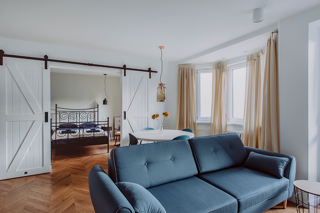 Blaues Sofa in einem offenen Wohnzimmer, das durch eine weiße Schiebetür vom Schlafzimmer getrennt ist