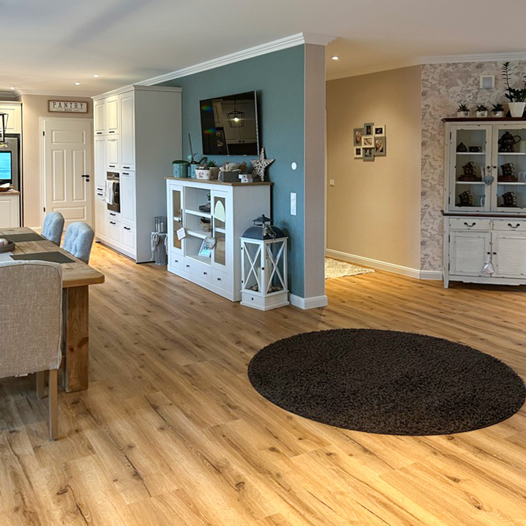 drewniana podłoga i białe meble w otwartej kuchni z jadalnią