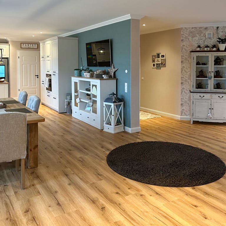 drewniana podłoga i białe meble w otwartej kuchni z jadalnią