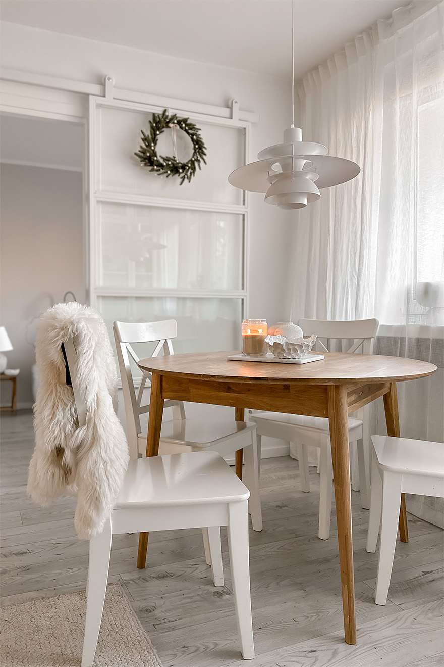 Weiße Stühle stehen um einen runden Holztisch im Wohnzimmer eines Wohnblocks