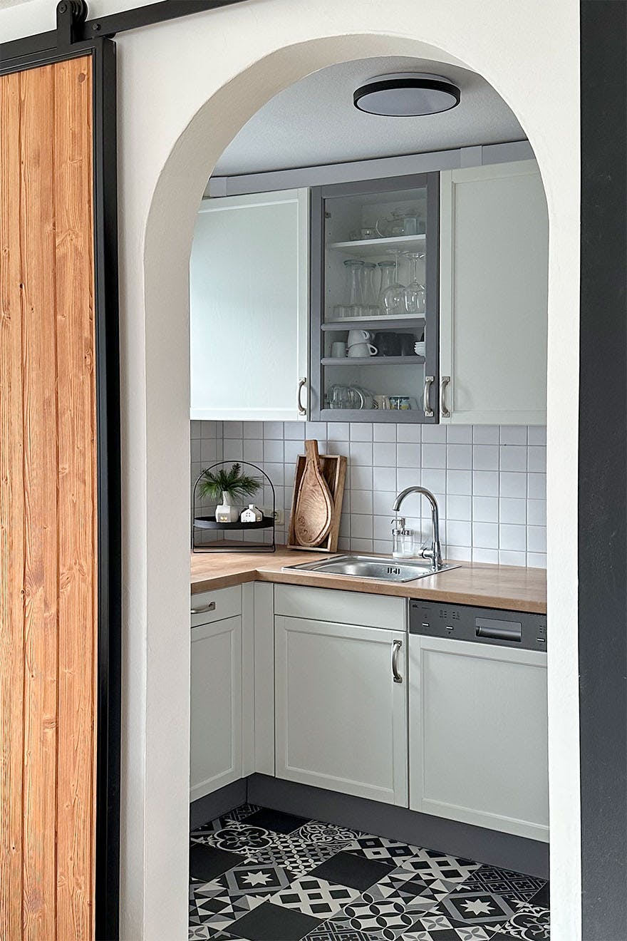 wejście do kuchni urządzonej w kolorach bieli i szarości z wzorzystą podłogą