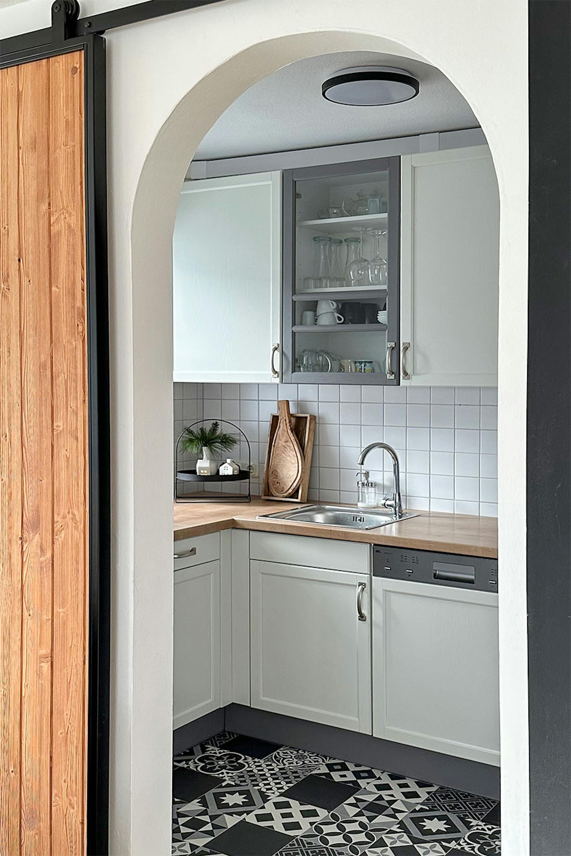 wejście do kuchni urządzonej w kolorach bieli i szarości z wzorzystą podłogą